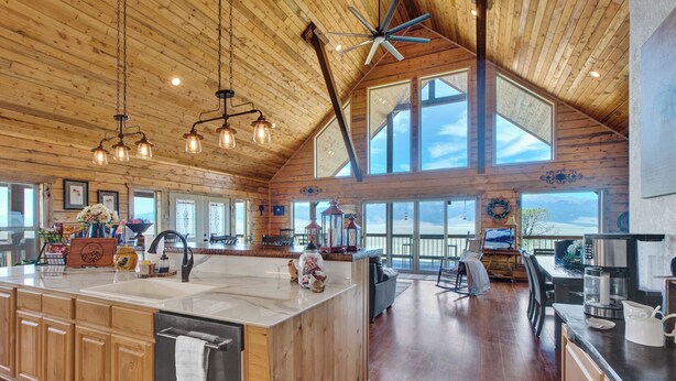 Une cuisine spacieuse avec des meubles en bois, un grand îlot central et un plafond haut avec des poutres apparentes.