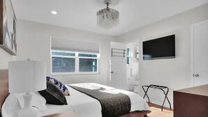 Een moderne slaapkamer met een groot bed, een aan de muur bevestigde televisie en een raam dat natuurlijk licht binnenlaat.