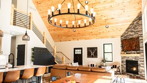 Een ruime woonkamer met een houten plafond, een stenen openhaard en een eettafel met stoelen.