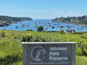 A sign for Johnson Field Preserve with a view of a harbor filled with boats. - Newly renovated home with water views in the heart of Bailey Island (Harpswell)
