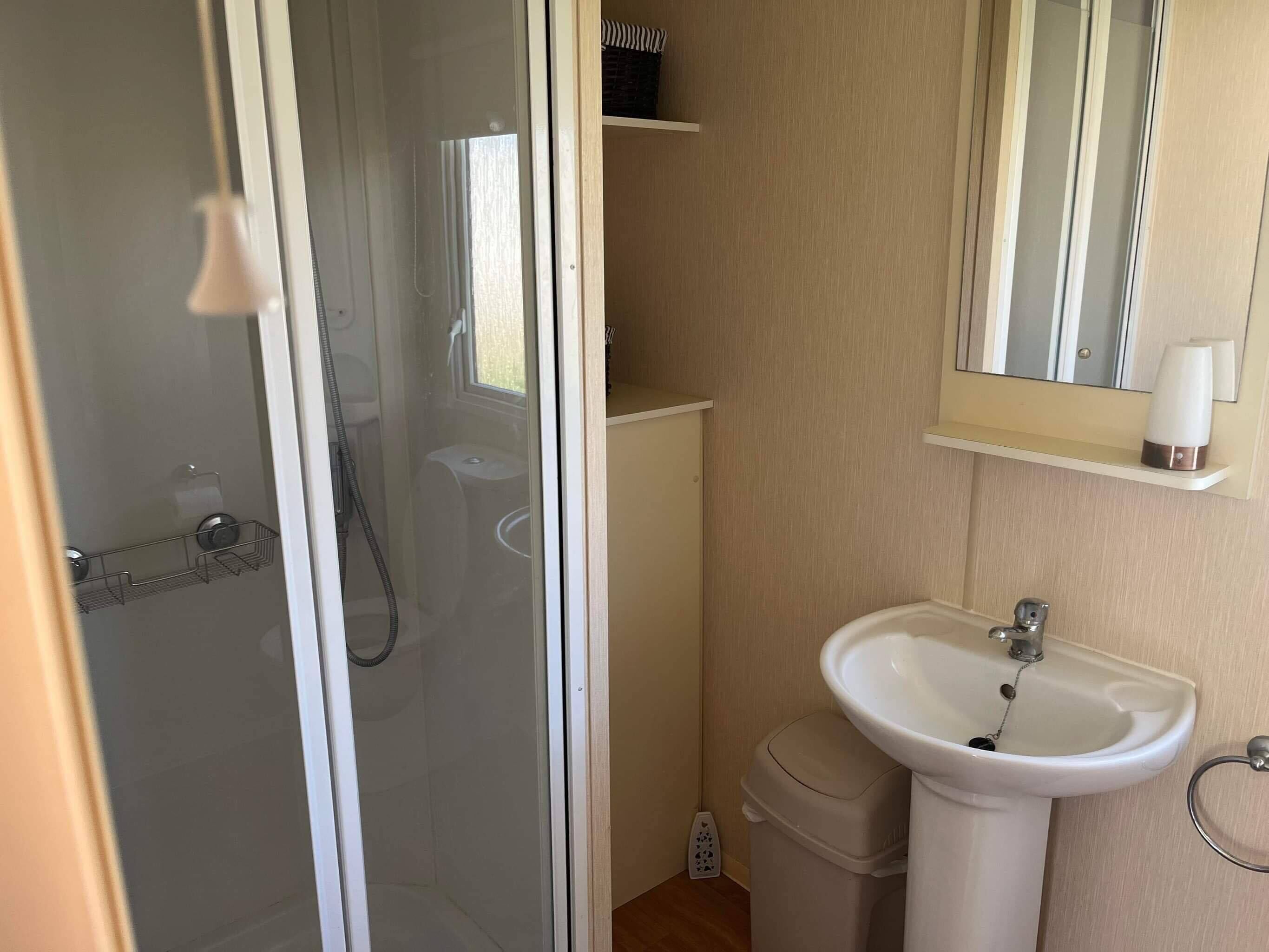 Un baño con ducha separada por mampara de vidrio, lavamanos y espejo.