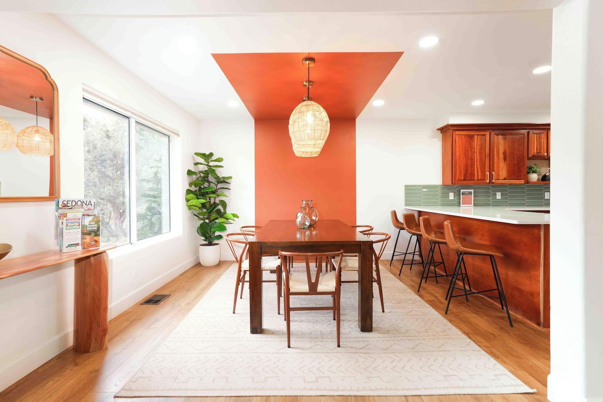 A modern kitchen with a wooden dining table, bar stools, and a large window.