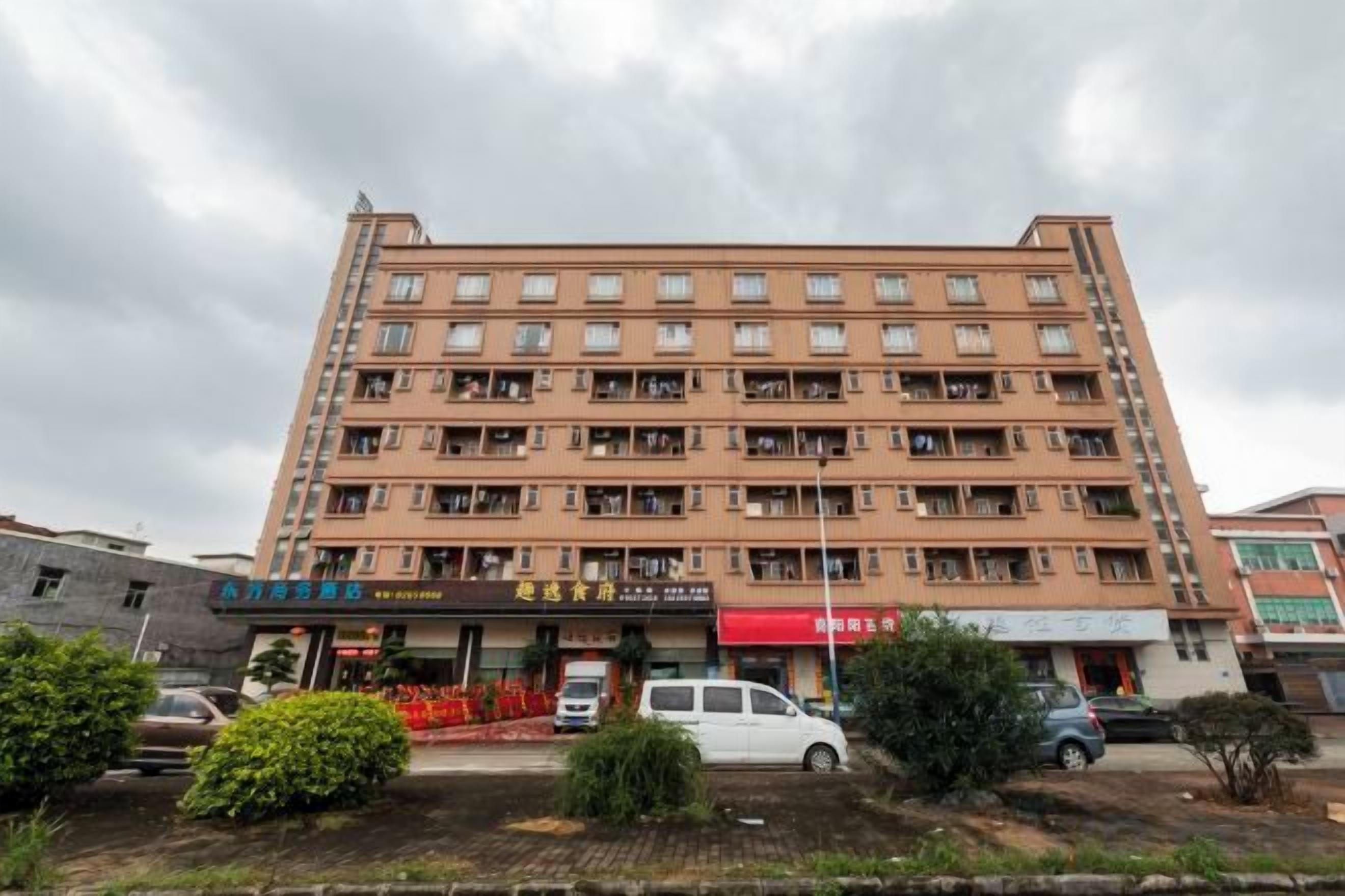 Ein mehrstöckiges Hotel mit schlichter Fassade, zahlreichen Balkonen und einem Ladenbereich im Erdgeschoss.