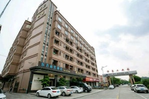 A multi-story hotel with a vertical entrance and several cars parked in front.