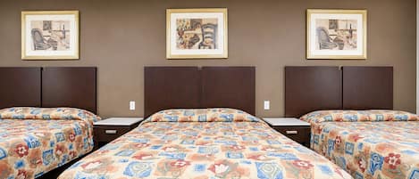 Habitación de hotel con tres camas, cada una con una colcha estampada, y tres cuadros enmarcados en la pared.