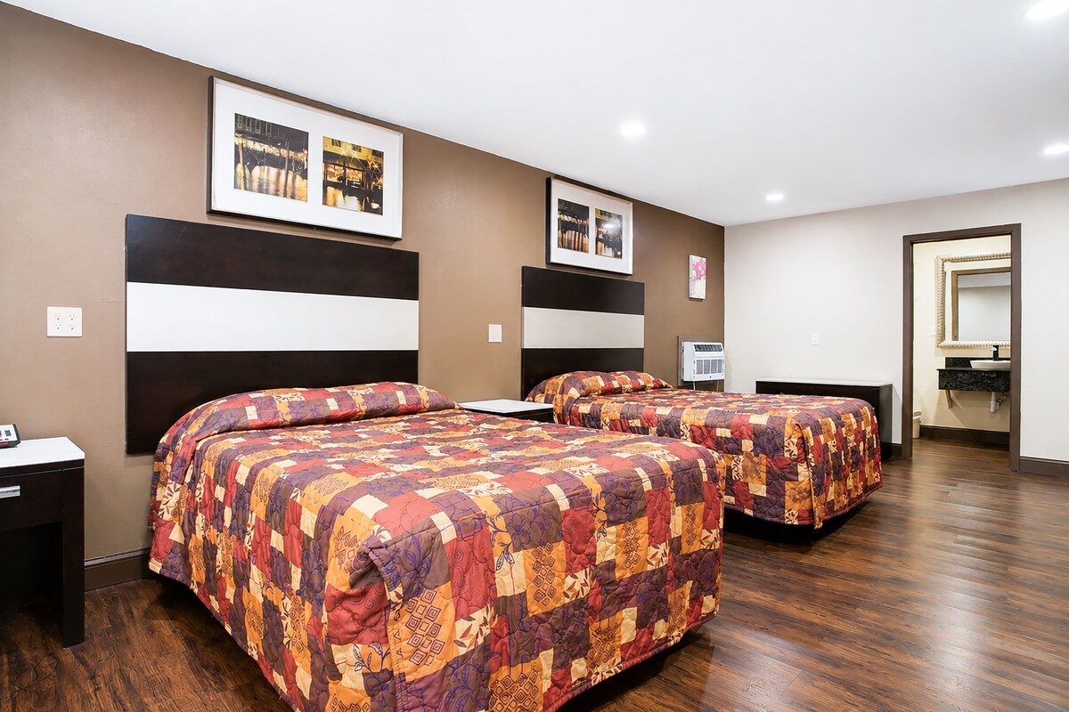 A hotel room with two beds, a nightstand, a mirror, and a framed picture on the wall.