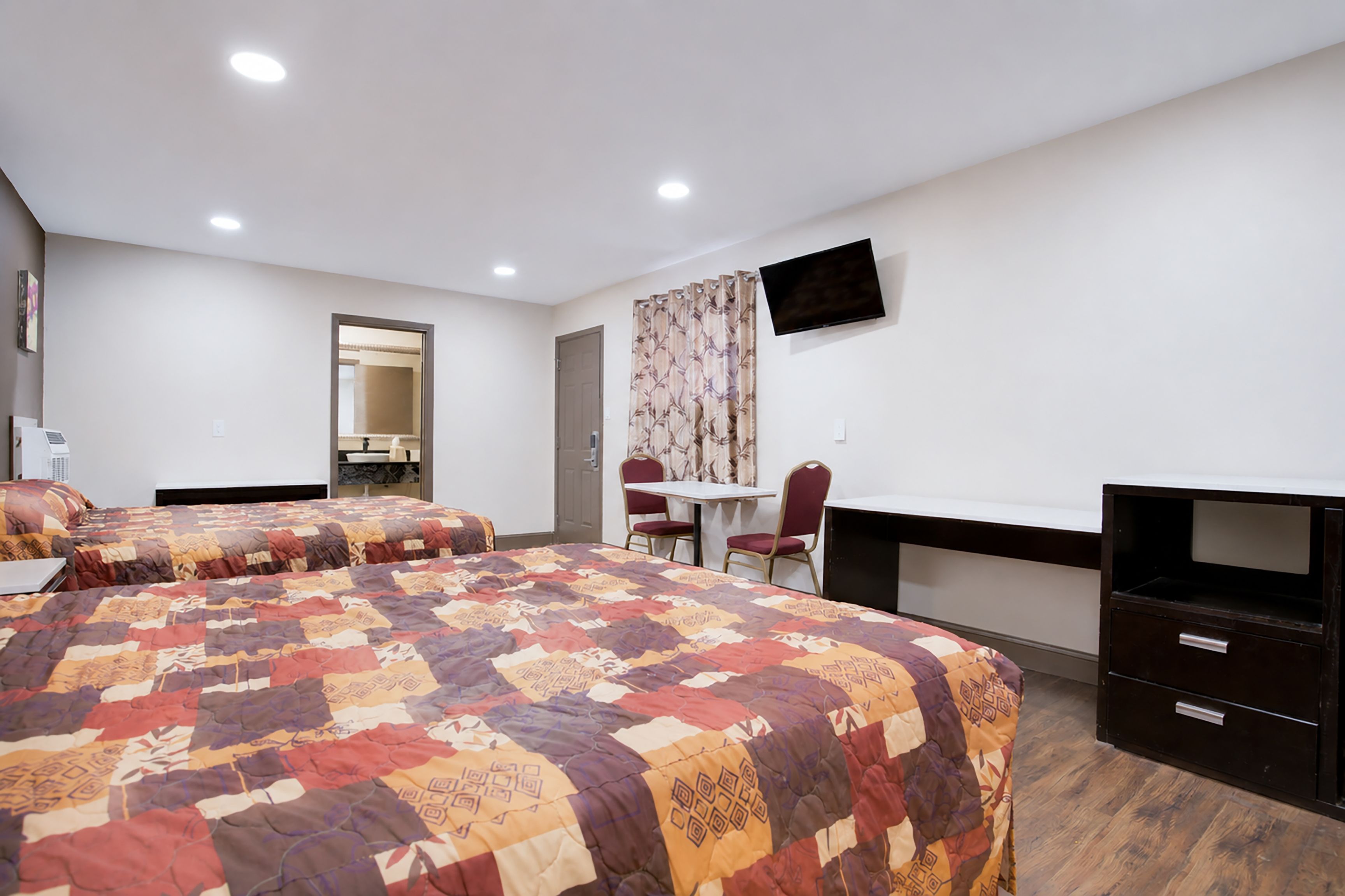 A hotel room with two beds, a desk, a chair, a television, and a mirror.