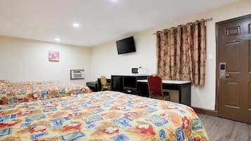 A hotel room with two beds, a desk with a computer, a TV, and a door.