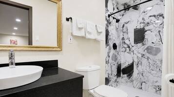 Une salle de bain avec un lavabo rond, des toilettes et une douche aux murs en marbre.