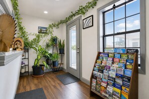Ein Korridor mit Holzboden, einer Tür, einem Fenster mit Blick und einer Wand mit Topfpflanzen und einem Informationsstand für Reisende.
