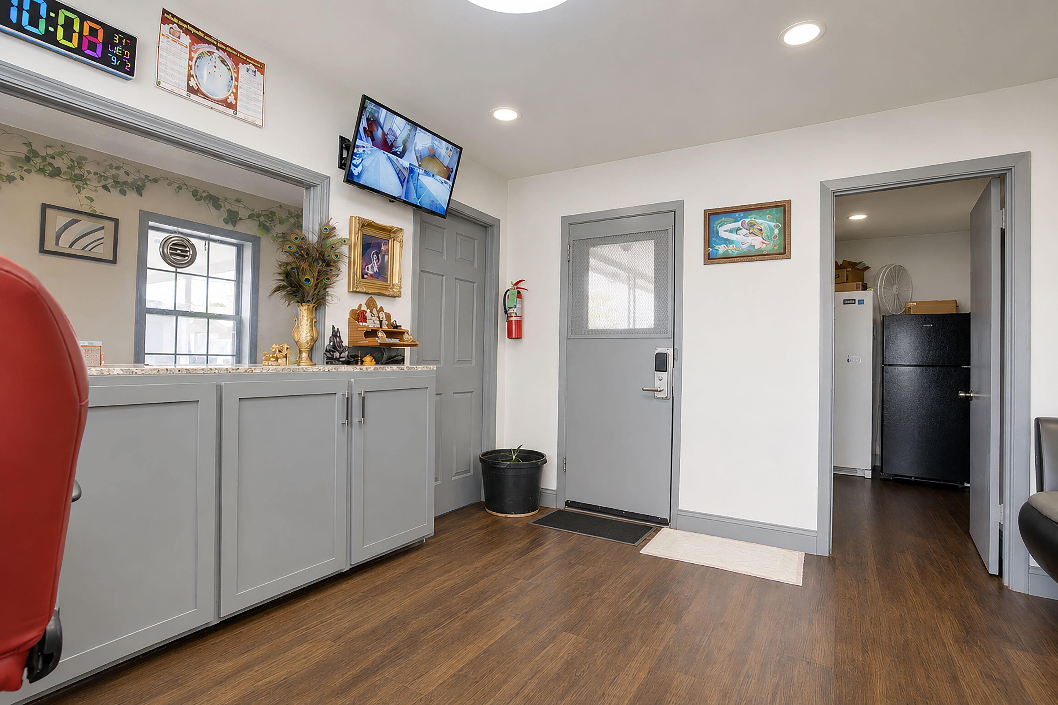 A kitchen with grey cabinets, a television mounted above the counter, and a door leading to another room.