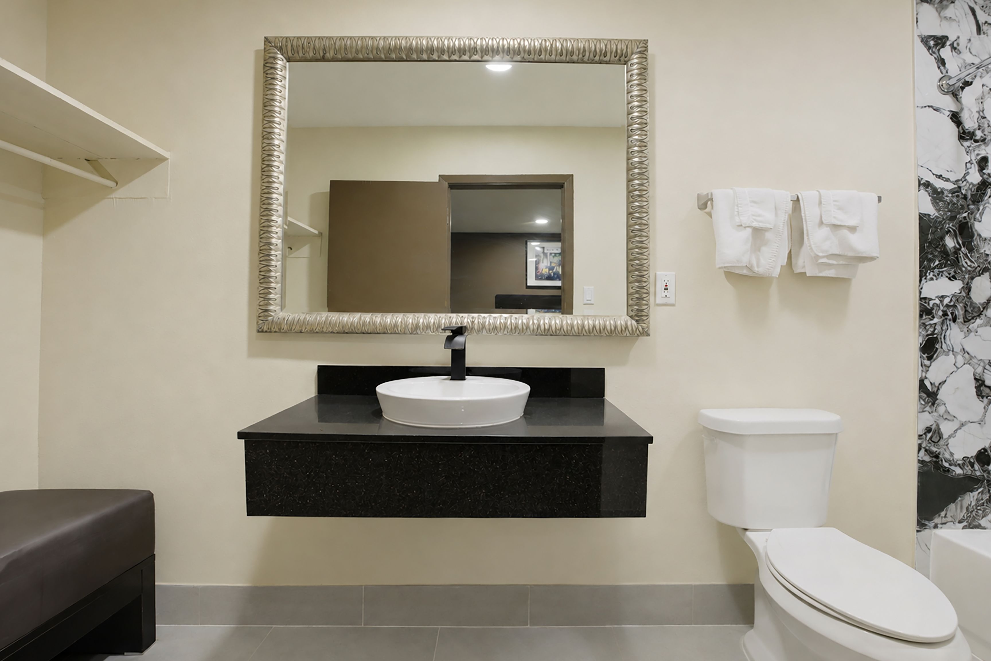 A bathroom with a black countertop, a white sink, a toilet, and a mirror with a decorative frame.