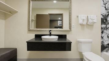 A bathroom with a black countertop, a white sink, a toilet, and a mirror with a decorative frame.