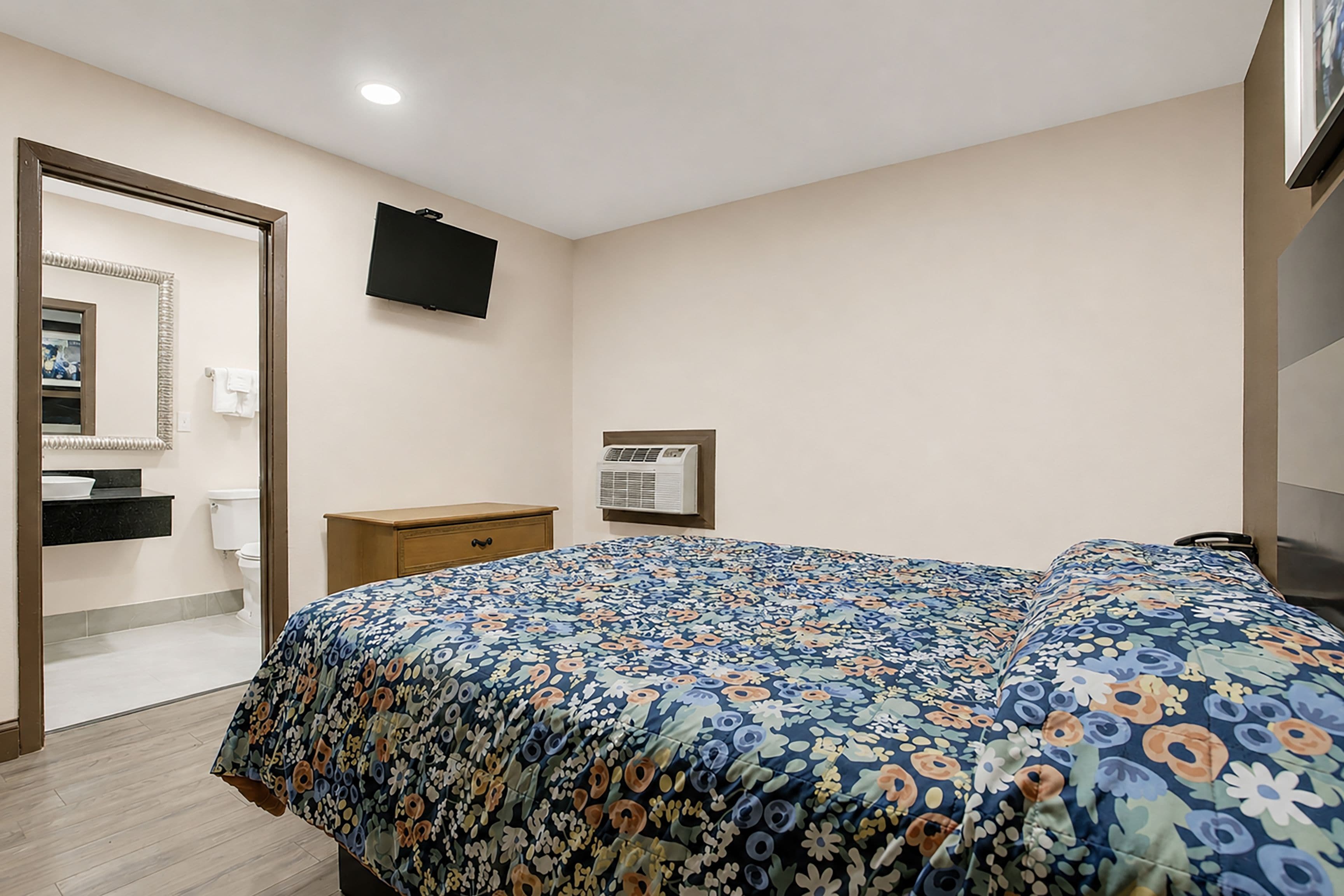 A bedroom with a bed, a dresser, a mirror, a television, and a window.