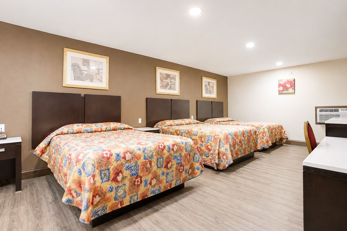 A hotel room with three beds, a desk, and a chair.