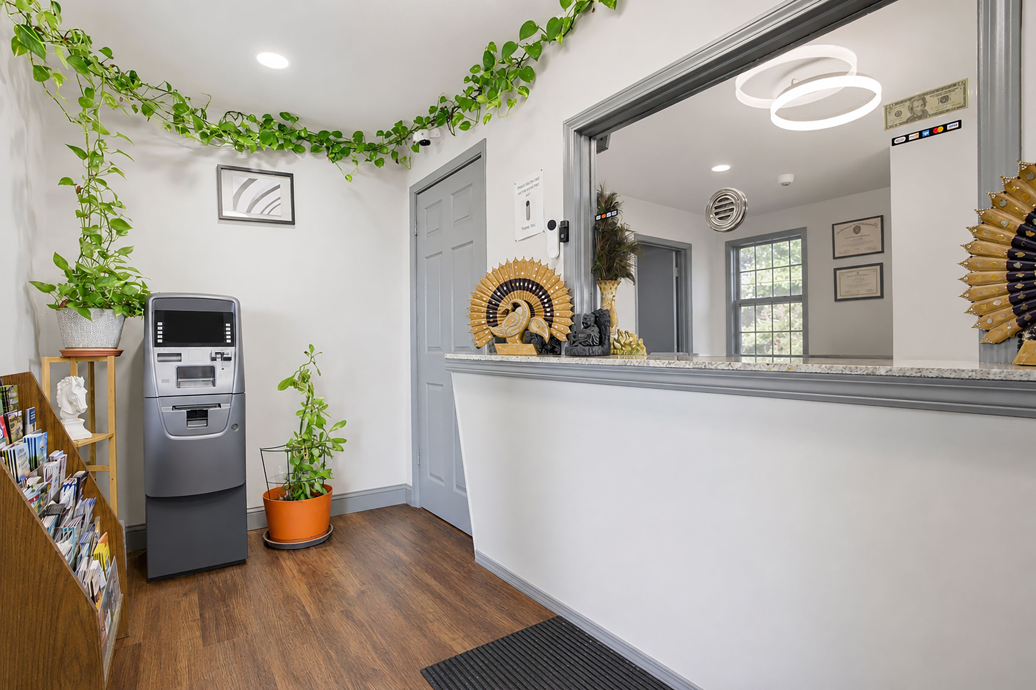Un espace d’accueil comprenant un distributeur automatique de billets, une plante en pot, un miroir décoratif et une porte.