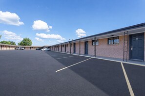 Um estacionamento com uma fileira de edifícios de motel térreo, cada um com porta e janelas.