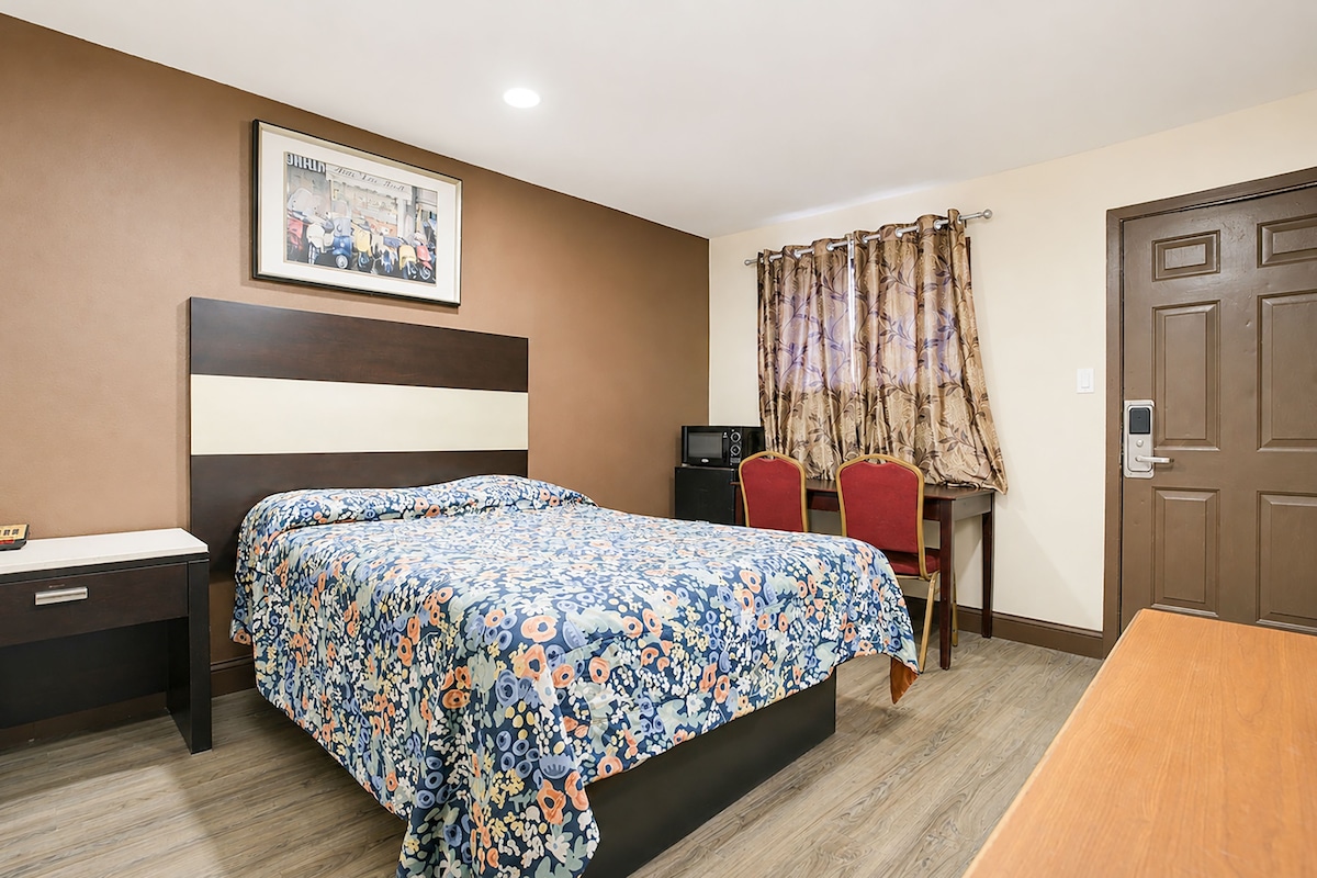 A hotel room with a bed, a desk, a chair, a television, and a door.