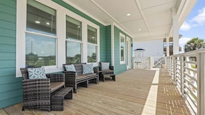 A covered outdoor seating area with wicker furniture and a wooden deck. - Beach View 4BR Retreat | Soccer Field | Putt-Putt | Pet Friendly (Galveston)