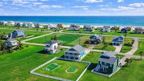 A coastal residential area with houses, a tennis court, and a view of the ocean. - Beach View 4BR Retreat | Soccer Field | Putt-Putt | Pet Friendly (Galveston)
