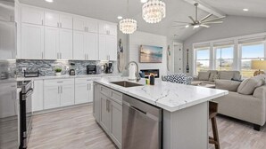 A modern kitchen with white cabinets, a marble countertop, and stainless steel appliances. There is a large island with a sink, and a ceiling fan above. - Beach View 4BR Retreat | Soccer Field | Putt-Putt | Pet Friendly (Galveston)