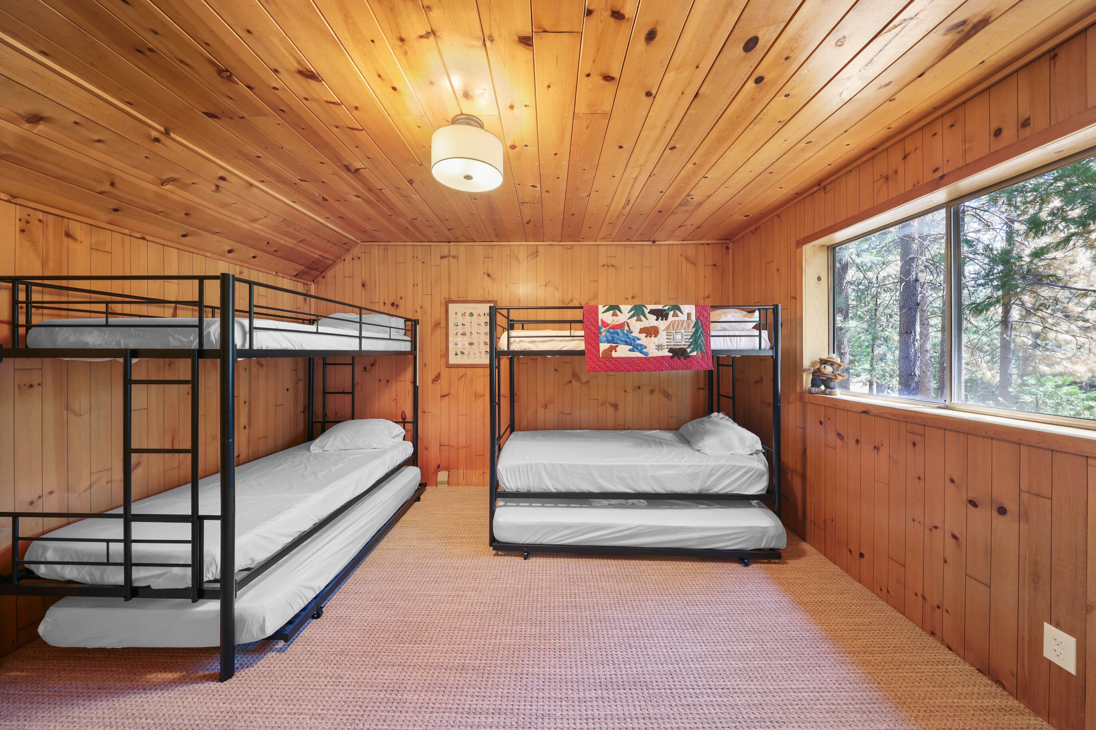 A cabin with wooden walls and floors, bunk beds, a window with a forest view, and a ceiling light.