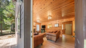 A wooden cabin interior with a wooden deck, two leather sofas, a television, and a door leading outside. - The Wildwood Cabin - Tahoe National Forest (Emigrant Gap)