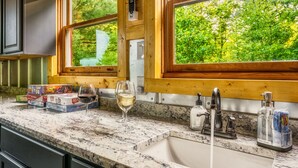 A kitchen with a marble countertop, a wine glass, a box of Tic Tac mints, a dish soap dispenser, and a window with a view of greenery. - Private*Pool*HotTub*Sauna*FirePit*Theater+GameRoom (Sevierville)