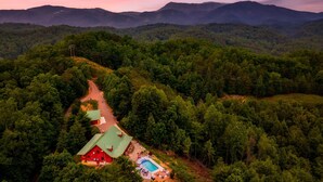 An aerial view of a cabin with a swimming pool surrounded by dense forest, set against a backdrop of mountains. - Private*Pool*HotTub*Sauna*FirePit*Theater+GameRoom (Sevierville)
