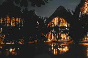 Un resort con varias construcciones, palmeras y una piscina reflectante de noche.
