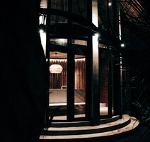 Un interior moderno con una zona de estar circular, una lámpara colgante y una escalera que sube a un nivel superior.