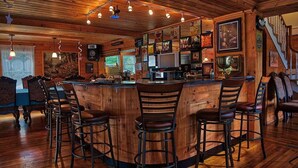 Uma área de bar com balcão de madeira, vários bancos e diversas fotos e decorações emolduradas nas paredes.