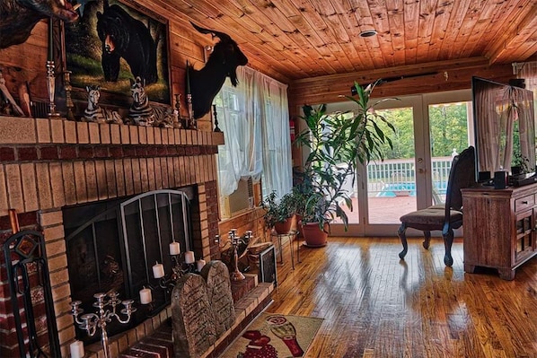 A cozy room with a fireplace, wooden ceiling, and a large window overlooking a deck.
