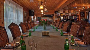Uma longa mesa de jantar posta para uma refeição em um quarto com paredes e teto de madeira, decorado com luzes em formato de estrela e um arranjo de flores.