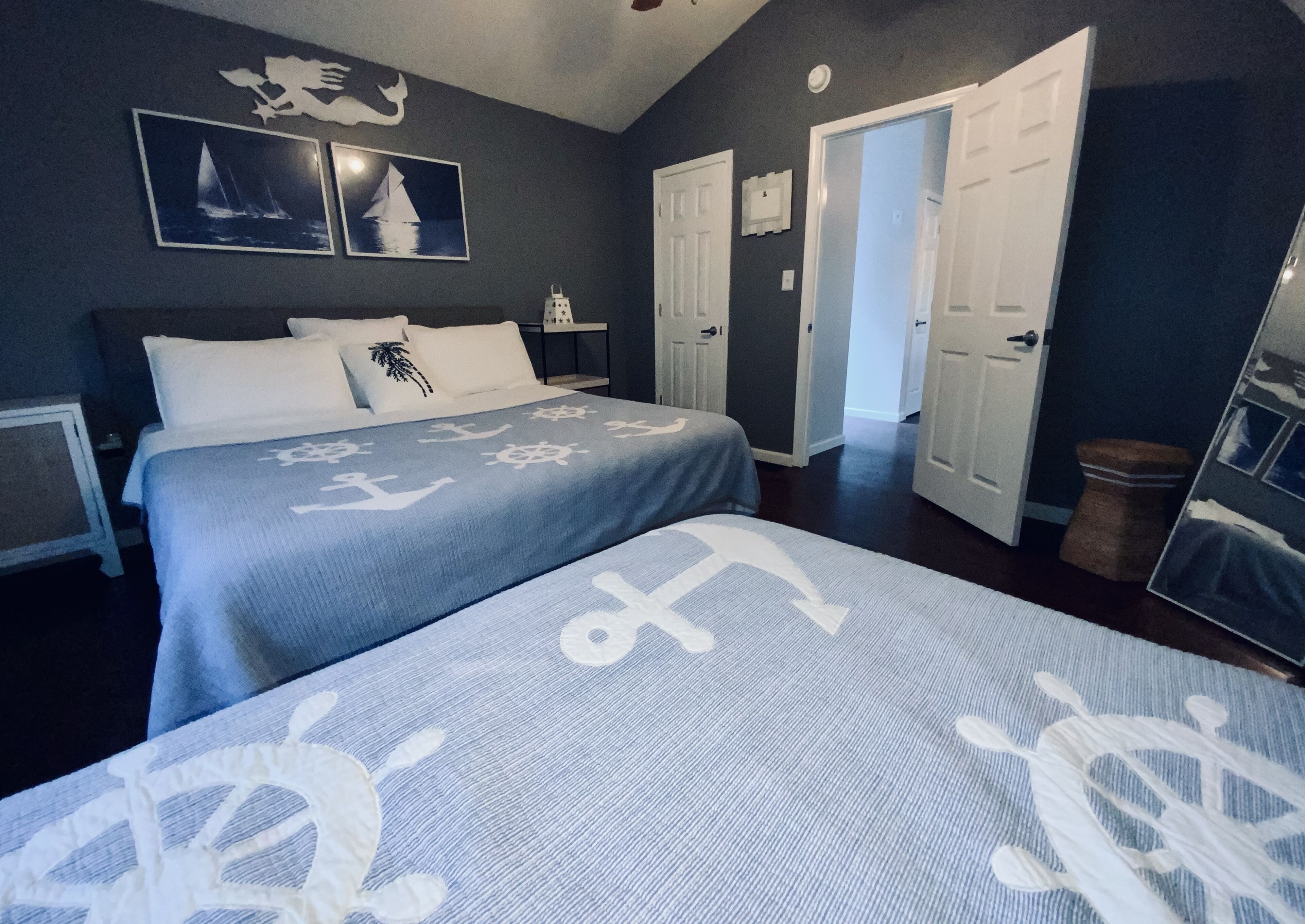 A bedroom with a bed, two nightstands, a dresser, and a door leading to another room.