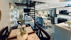 Une cuisine moderne équipée d’un four à micro-ondes, d’un réfrigérateur et d’une cuisinière intégrés. On y trouve également un coin repas avec une table pour deux personnes et une plante en pot.