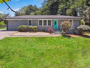 A single-story house with a front porch, a green door, and a small front yard with a gravel area and a lawn.