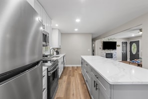 A modern kitchen with stainless steel appliances, a marble countertop, and a wooden floor.