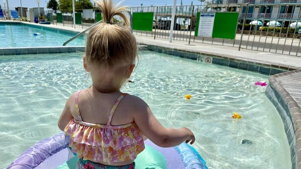 A child on a pool float in a swimming pool area with clear water, a fence, and a building in the background. - The VIP Family Motel (Wildwood Crest)
