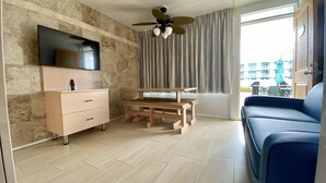 A modern living room with a flat-screen TV, wooden furniture, a ceiling fan, and a view of the outside. - The VIP Family Motel (Wildwood Crest)