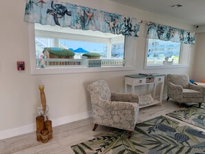 A room with two windows, a white console table, two patterned armchairs, a wooden sculpture, and a green patterned rug. - The VIP Family Motel (Wildwood Crest)