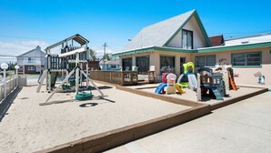 A playground with swings and slides, a wooden deck, and a building with a green roof and windows. - The VIP Family Motel (Wildwood Crest)