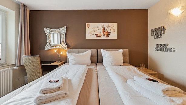 A hotel room with two beds, a nightstand, a lamp, a mirror, a painting, and a motivational wall quote. - 7o'Clock Hotel Hannover Messe Laatzen (Laatzen)