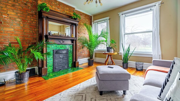 A living room with a brick fireplace, wooden flooring, and a grey sofa. - The Parkside by Jungle House – Short North Boutique Suites (Columbus)