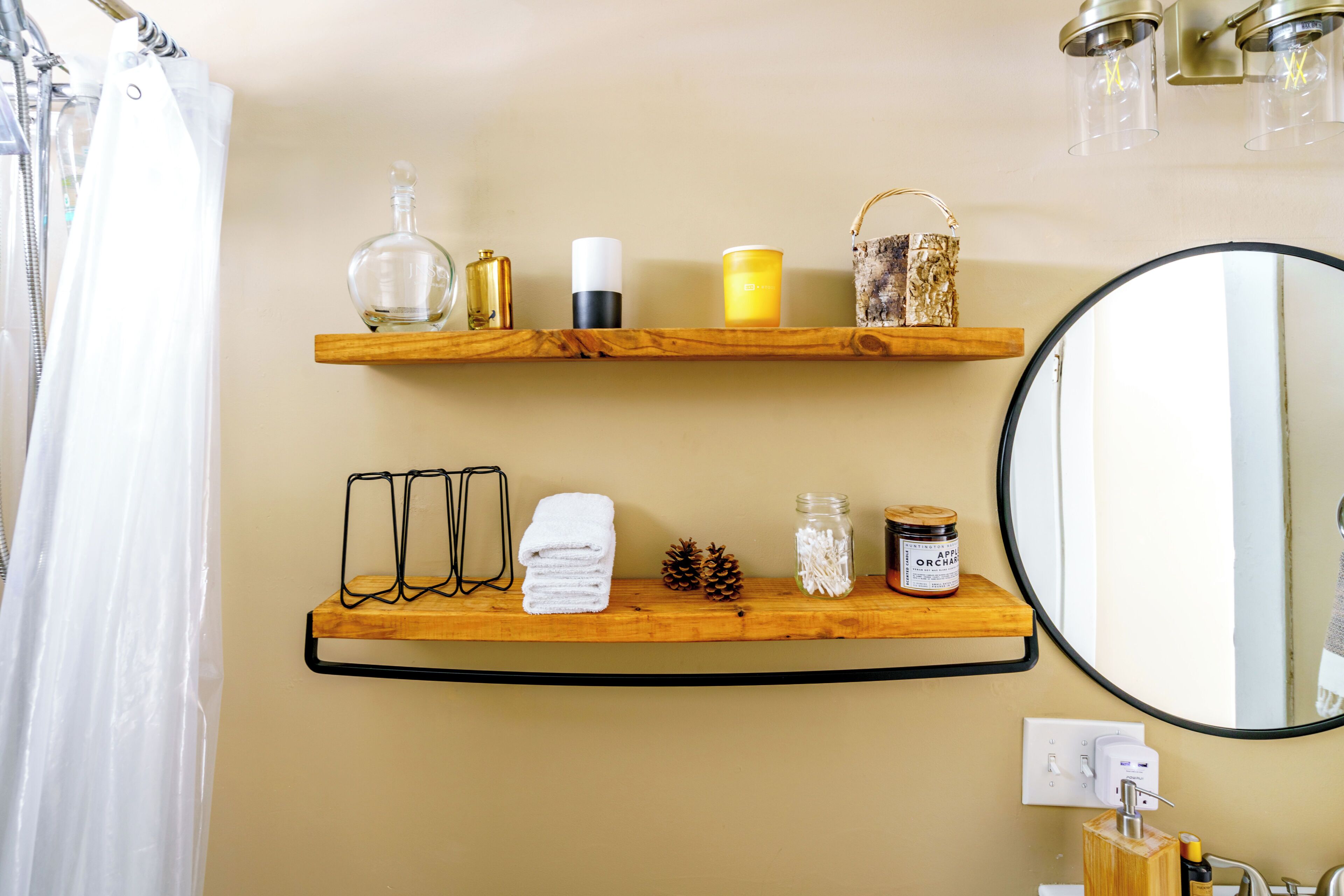 A bathroom with wooden shelves holding toiletries, a mirror, and a shower curtain.