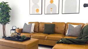 Un salon avec un canapé en cuir marron, une table basse et un tapis à rayures. Trois œuvres d’art abstraites sont accrochées au mur au-dessus du canapé.