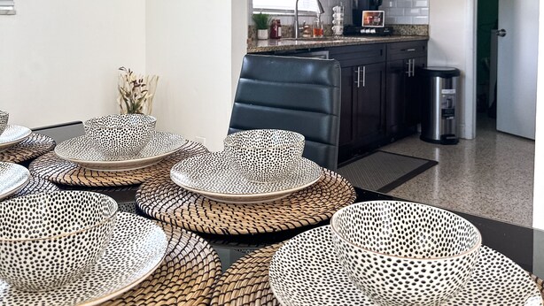 Une cuisine moderne avec des meubles de couleur sombre, une chaise noire et une table à manger agrémentée de sets de table en fibres tressées.