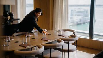 A conference room with a large table, chairs, and a view of a cityscape through large windows.