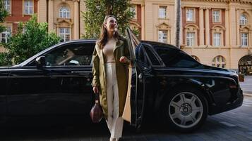 A woman exiting a black luxury car parked in front of a historic building with classical architecture.