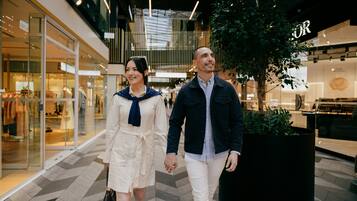A couple walking in a modern shopping mall with glass storefronts and indoor plants.